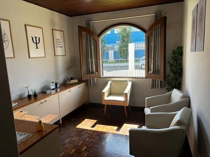 Consultório da Mirian em Ponta Grossa: sala com janela arqueada, poltronas claras, samambaia e quadros na parede